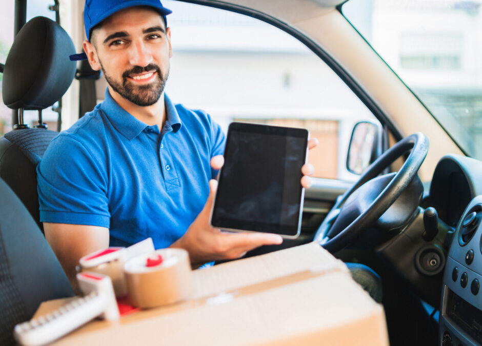 Delivery driver holding a tablet inside a commercial vehicle with packages in the foreground.
